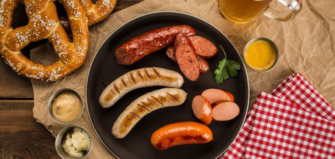 Oktoberfestmåltid med kringlor, korvar, senap och öl på träbord