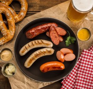 Oktoberfestmåltid med kringlor, korvar, senap och öl på träbord