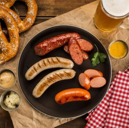 Oktoberfestmåltid med kringlor, korvar, senap och öl på träbord