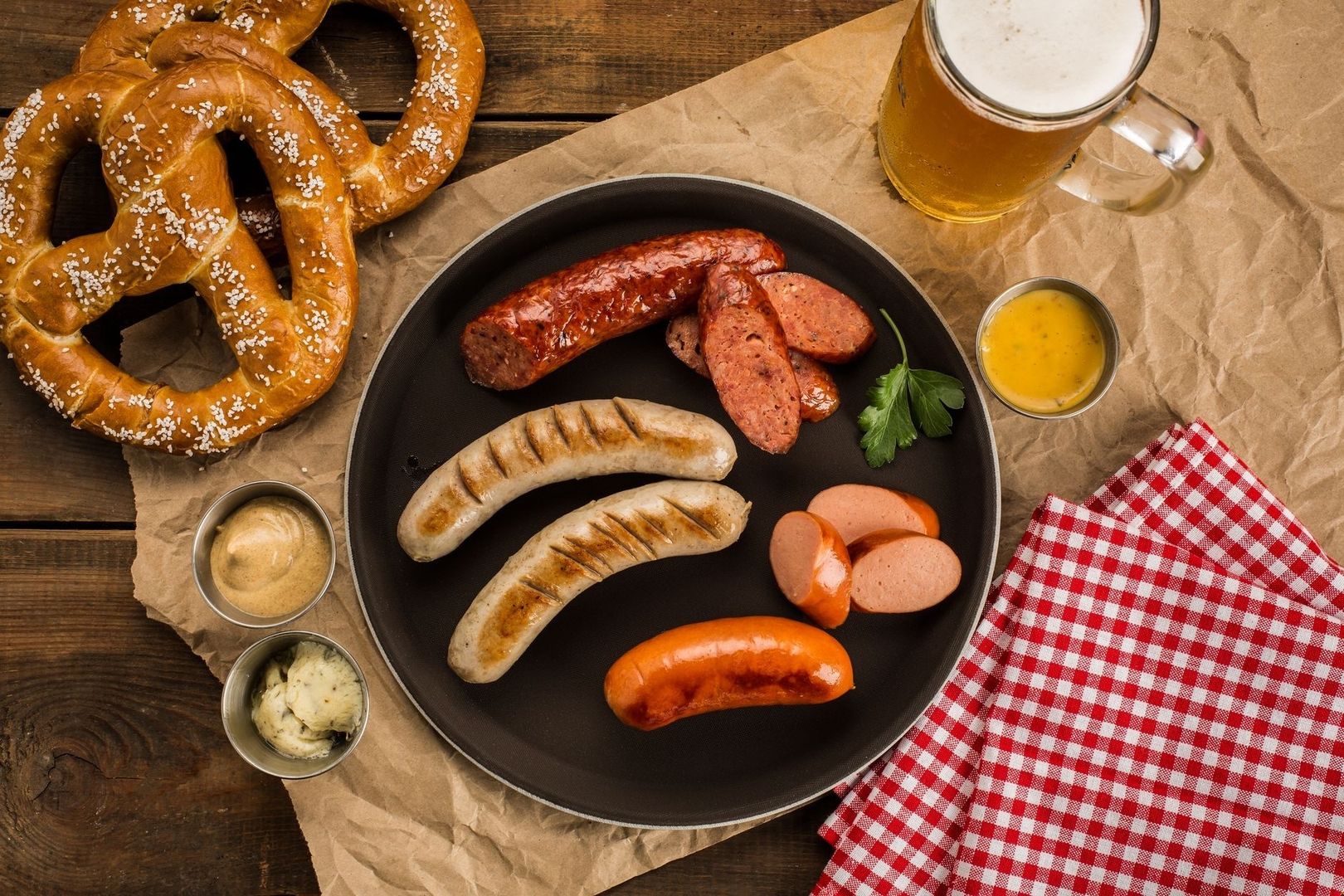 Oktoberfestmåltid med kringlor, korvar, senap och öl på träbord